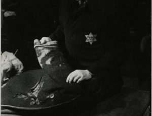 Muž s židovskou hvězdou prohlíží obnošený kabát (zdroj: http://collections.jewishmuseum.cz)